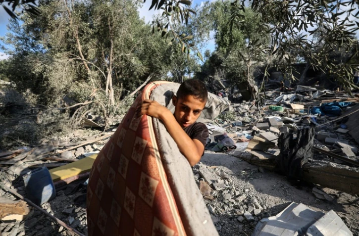 Un garçon palestinien récupère un matelas des décombres d'une maison après une frappe israélienne nocturne qui a touché Nousseirat, dans le centre de la bande de Gaza, le 13 juillet 2025