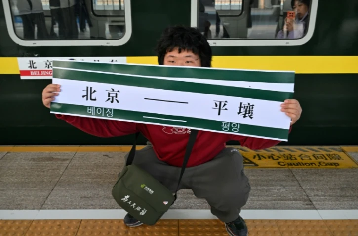 Un homme brandit une banderole "Pékin-Pyongyang" devant le train K27 à destination de Pyongyang, à la gare de Pékin, le 12 mars 2026 en Chine