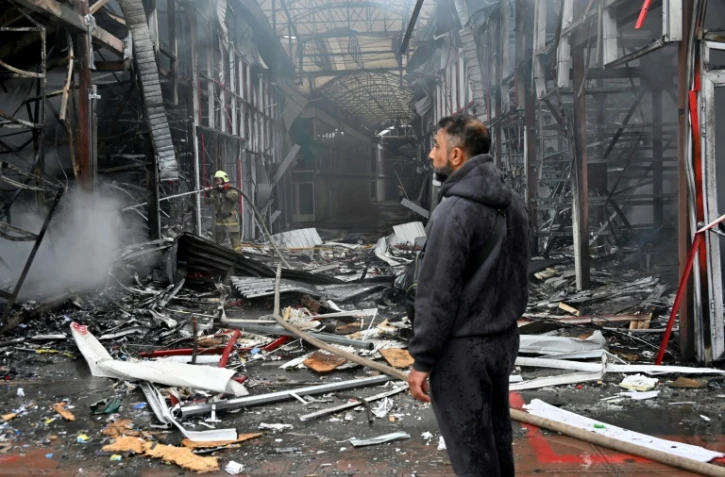 Un homme observe les dégâts alors qu'un pompier ukrainien éteint un incendie au marché "Barabashovo" après une attaque de drone à Kharkiv, le 6 mai 2025 en Ukraine