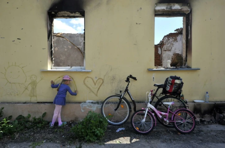 Une jeune fille dessine sur le mur d'une maison détruite à Andriivka, dans la région de Kiev, le 3 juin 2022
