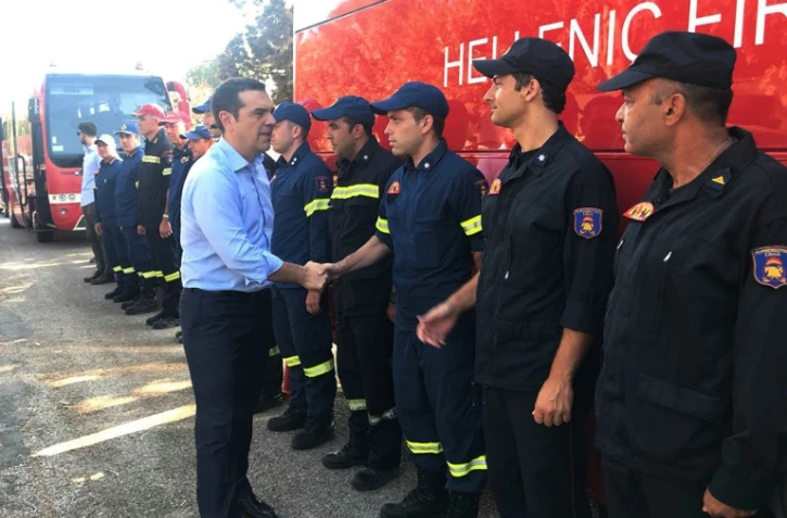 Le Premier ministre grec Alexis Tsipras (c) salue les pompiers ayant combattu les incendies meurtriers de Mati, à l'est d'Athènes, le 30 juillet 2018