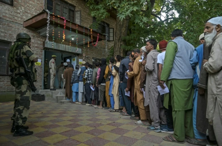 Un agent de sécurité indien monte la garde alors que les électeurs font la queue pour voter dans un bureau de vote lors de la première phase des élections législatives à Pulwama, au sud de Srinagar, le 18 septembre 2024