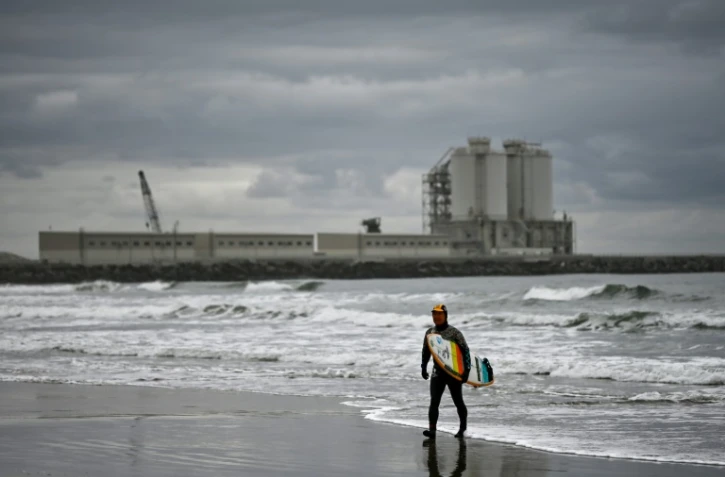 Koji Suzuki, un surfeur japonais, marche sur la plage de Minamisoma devant une centrale thermique, à une trentaine de km au nord de la centrale nucléaire de Fukushima Daiichi, le 4 mars 2020 