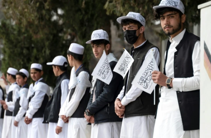 Des élèves tiennent des drapeaux talibans pendant une cérémonie marquant la rentrée scolaire,à l'école Amani de Kaboul, le 20 mars 2024 en Afghanistan
