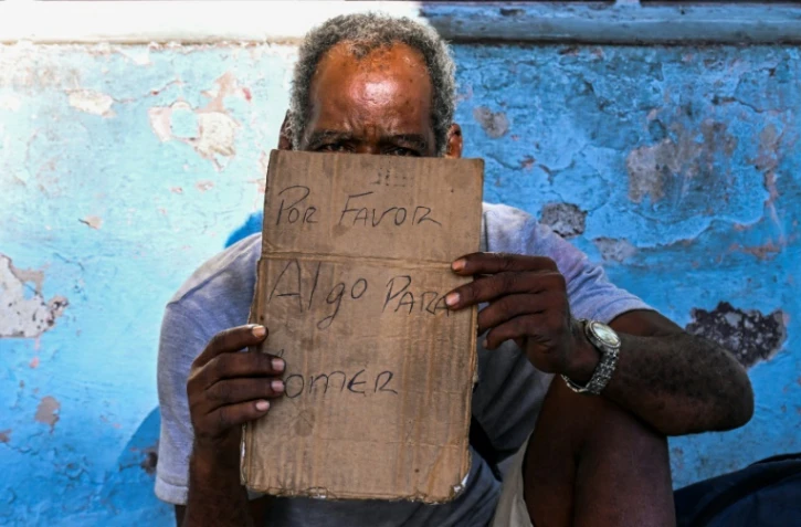 Un homme tient un morceau de carton sur lequel est écrit "S'il vous plaît, pour manger", alors qu'il mendie dans une rue de La Havane, le 21 juillet 2025 à Cuba