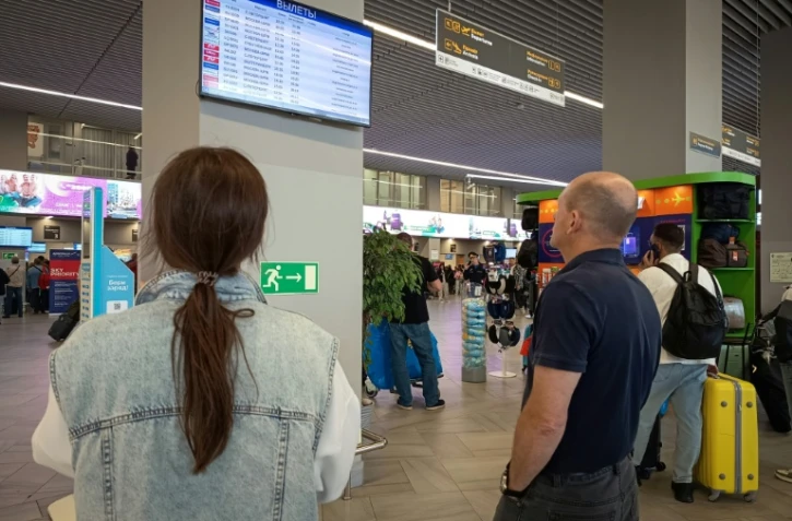 Des passagers regardent un panneau d'affichage des vols à l'aéroport de Kaliningrad, en Russie, le 4 juillet 2026