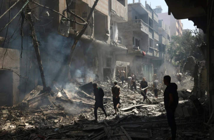 Des Palestiniens marchent le 8 juin 2024 dans des gravats de bâtiments détruits lors d'une opération israélienne pour libérer des otages à Nousseirat, dans le centre de la bande de Gaza, où une guerre oppose Israël au mouvement islamiste Hamas
