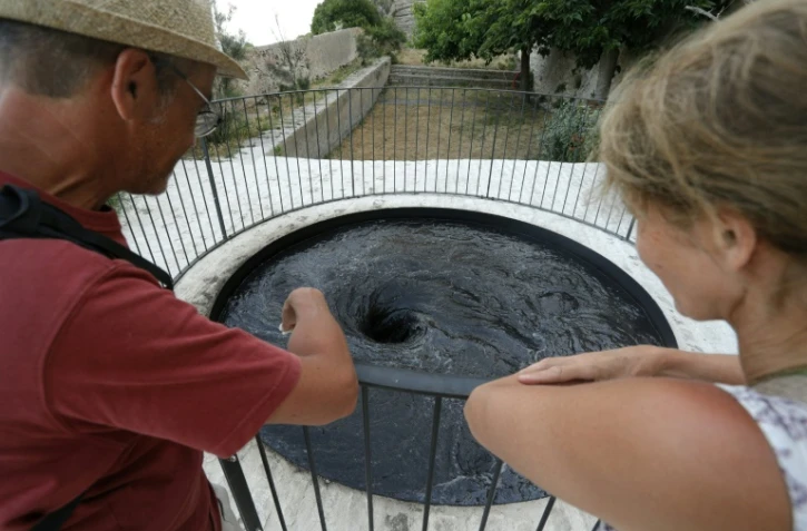 Des touristes devant l'oeuvre du plasticien britannique Anish Kapoor intitulée "Descension" à la Biennale d'art contemporain de Bonifacio, en Corse-du-Sud, le 21 juin 2022