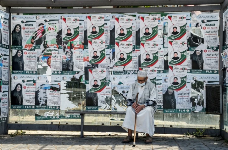 Un homme assis dans un abribus recouvert d'affiches électorales à Algers, le 11 juin 2021, à la veille des élections législatives