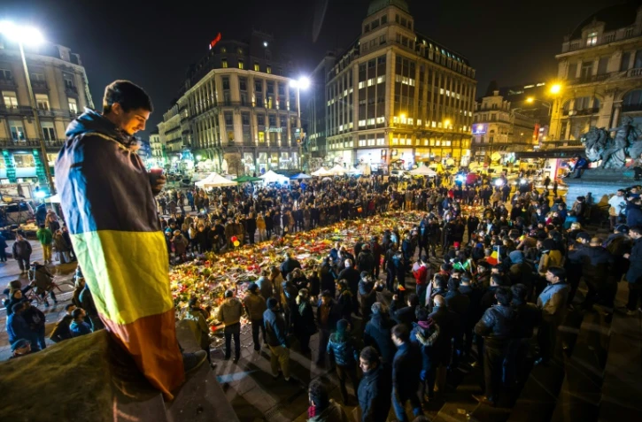Un homme enveloppé dans un drapeau belge tient une bougie place de la Bourse, à Bruxelles, le 24 mars 2016, en hommage aux victimes des attentats de l'aéroport de Zaventem et du métro bruxellois
