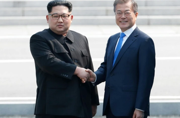 Moon Jae-in (d) et Kim Jong Un se serrent la main sur la ligne de démarcation avant le début du sommet, le 27 avril 2018 à Panmunjom
