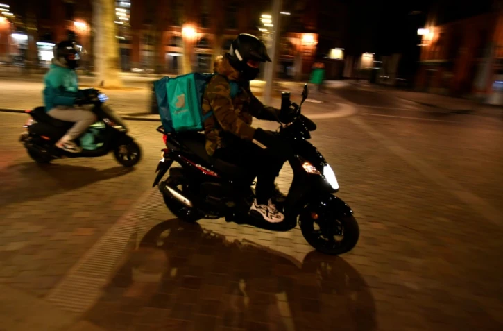 Deux liveurs à scooter Deliveroo traversent la Place Saint Pierre à Toulouse, le 16 janvier 2021