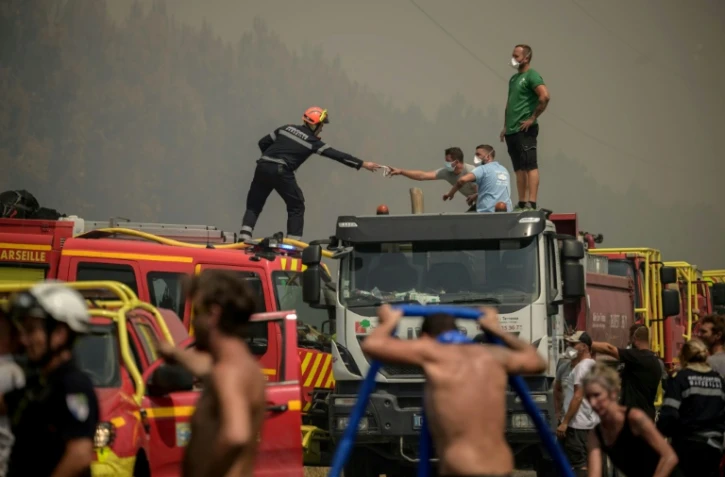 Un pompier tend un masque Ă un volontaire en pleine lutte contre un feu de forĂŞt Ă Lanton, Ă l'est du bassin d'Arcachon et Ă l'ouest de Bordeaux, le 29 juillet 2026