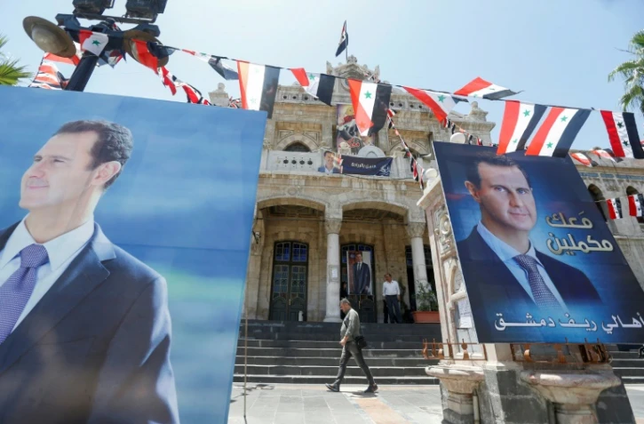 Des passants passent devant des affiches électorales de Bachar al-Assad, le 25 mai 2021 à Damas.
