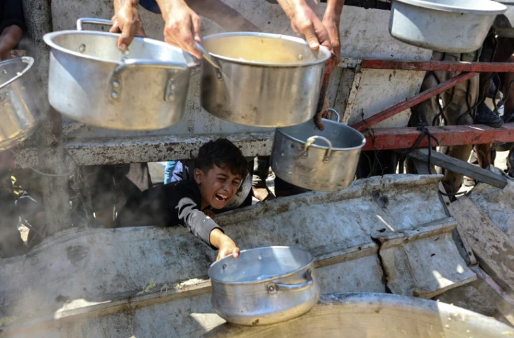 Un garçon palestinien tend une casserole vide devant une organisation de charité locale distribuant du riz cuit, dans la ville de Gaza, le 23 août 2025