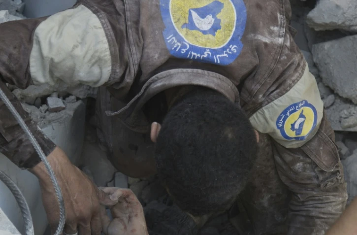 Un volontaire de la défense civile syrienne dégage un garçon coincé dans les décombres d'un immeuble, le 25 juillet 2016 à Alep, dans le nord de la Syrie