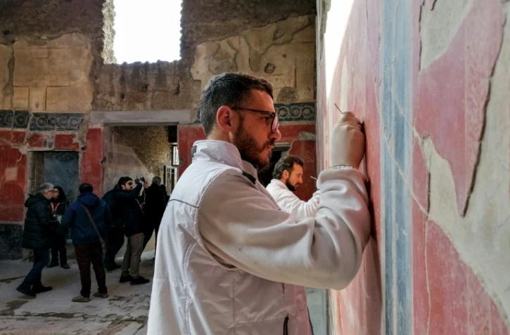Photo prise le 18 février 2020 montrant un restaurateur nettoyant une fresque de "La maison des chastes amants" à Pompéi