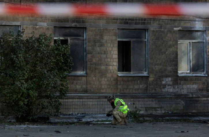 Un policier ukrainien inspecte des débris près d'un bâtiment endommagé par une frappe de drone russe à Kiev, le 1er octobre 2026