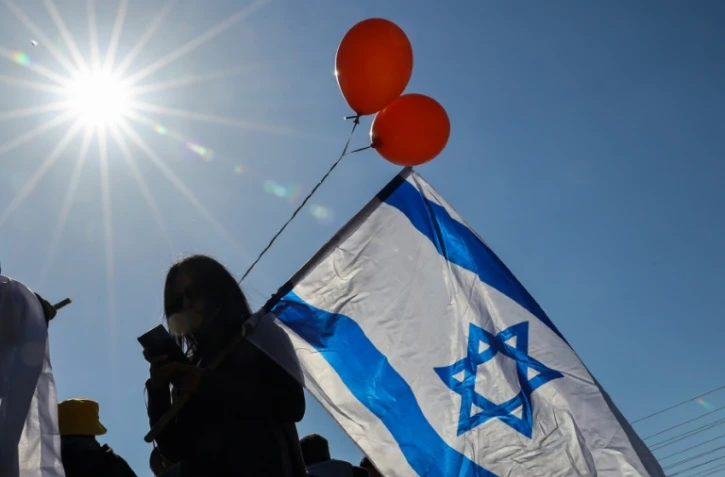 Des Israéliens portant le drapeau national et des ballons orange attendent l'arrivée du convoi funéraire de la famille Bibas, dans le kibboutz Nir Oz, dans le sud d'Israël, le 26 février 2025