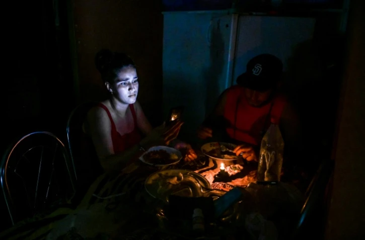 Une femme consulte son téléphone tout en dînant à la bougie pendant une coupure de courant, le 25 mai 2022 à La Havane