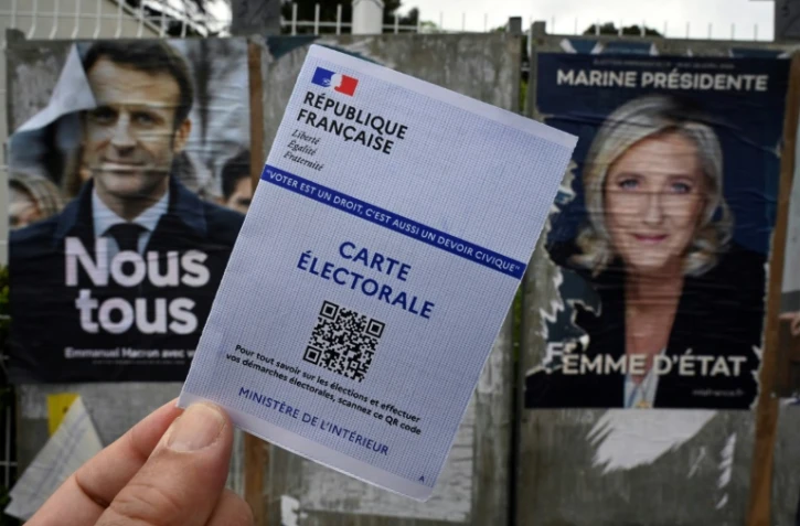 Une carte électorale devant des affiches de la candidate du parti d'extrême droite Rassemblement National, Marine Le Pen (D), et du président sortant et candidat à sa réélection, Emmanuel Macron (G), à Montpellier, dans le sud de la France, le 21 avril 2022