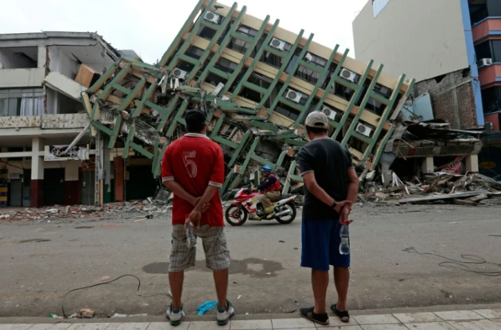 Deux hommes regardent un immeuble détruit à Portoviejo, en Equateur, le 21 avril 2016, une semaine après le violent séisme qui a ravagé le pays