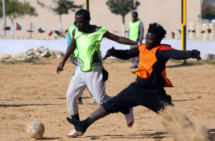 Des migrants Camerounais (orange) et Sénégalais (jaune) participent à un match de football au camp de Tarjoura en Libye, le 28 février 2018