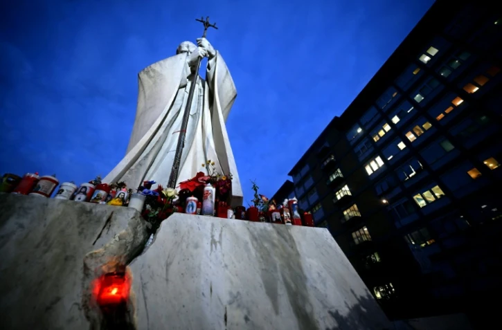 Des fleurs et des bougies déposées au pied d'une statue de Jean-Paul II devant l'hôpital Gemelli où est hospitalisé le pape François, le 20 février 2025 à Rome