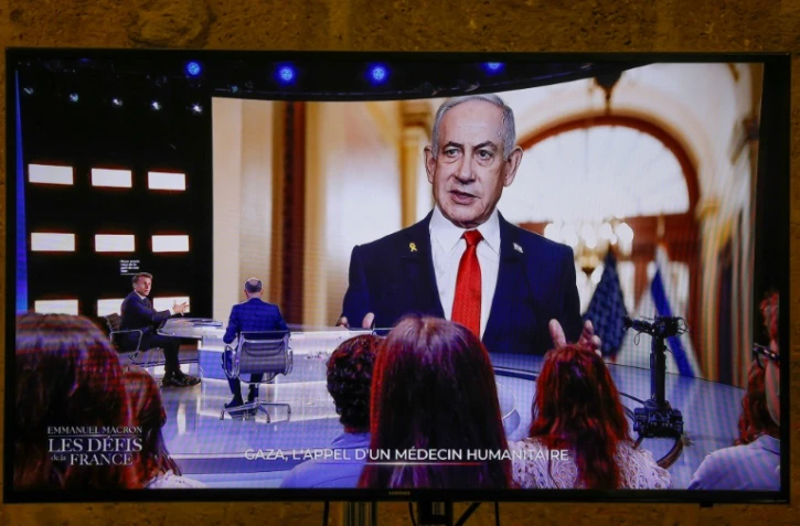 Cette photo prise sur un écran de TF1, montre le président français Emmanuel Macron, alors qu'une photo du Premier ministre israélien Benjamin Netanyahu s'affiche en arrière-plan, lors d'une émission dans les studios de télévision de Saint-Denis, le 13 mai 2025
