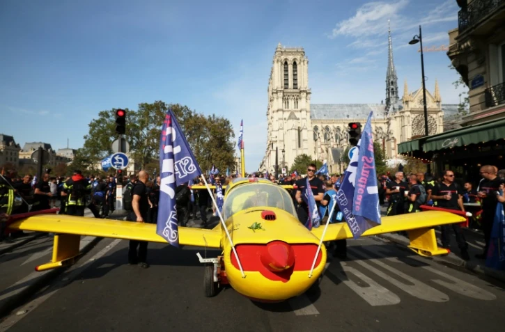 Des pompiers installent un avion peint aux couleurs de la Sécurité civile devant la cathédrale Notre-Dame de Paris, lors d'une manifestation pour réclamer des hausses de salaires et des moyens budgétaires accrus, le 28 septembre 2026 à Paris