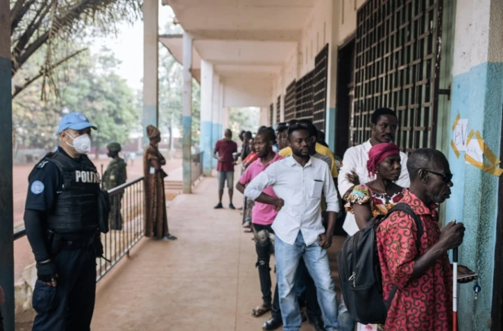 Des électeurs font la queue devant un bureau de vote de Bangui, sous l'oeil d'un policier de la Minusca, le 27 décembre 2020