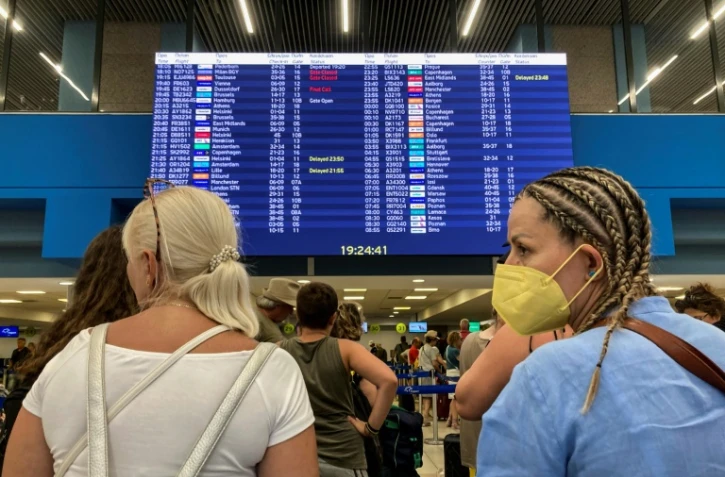 Des touristes fuuyant les incendies dans l'île de Rhodes en attente devant un panneau d'affichage des vols à l'aéroport de l'île grecque en  proie à des incendies sans précédent le 23 juillet 2023
