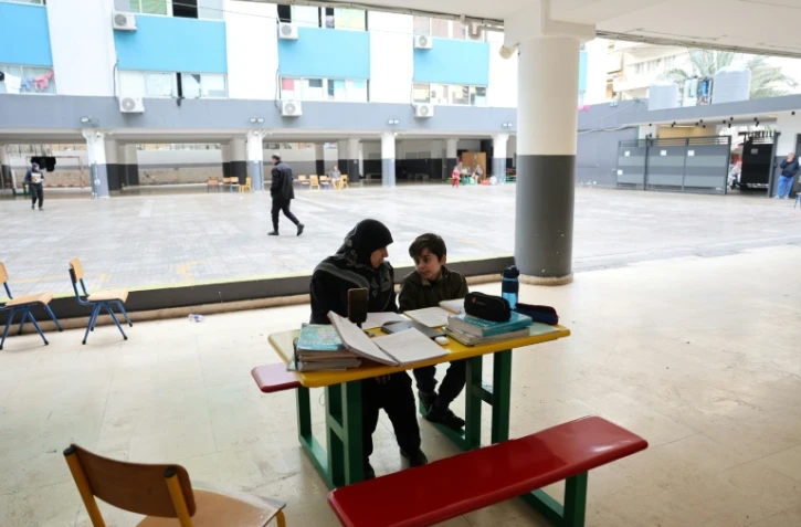 Une femme, assise à côté d'un enfant, supervise ses études en ligne sur un téléphone portable dans une école publique transformée en refuge pour personnes déplacées, à Dekwaneh, au nord de Beyrouth, le 25 mars 2026 au Liban