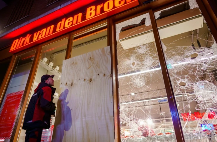 Un homme se tient devant la vitrine brisée d'un supermarché à la suite d'émeutes à Rotterdam, le 25 janvier 2021