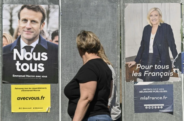 Femme passant deux affiches d'Emmanuel Macron et Marine Le Pen, à Eguisheim (Haut-Rhin), le 21 avril 2022