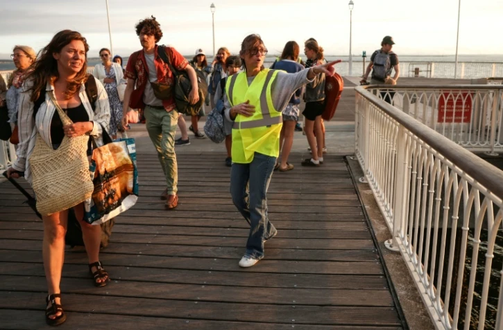 Une bénévole donne des instructions aux vacanciers de Lège-Cap-Ferret à leur arrivée à Arcachon par bateau, lors d'une opération d'évacuation de l'ensemble de la presqu'île du Cap-Ferret, dans le sud-ouest de la France, le 24 juillet 2026