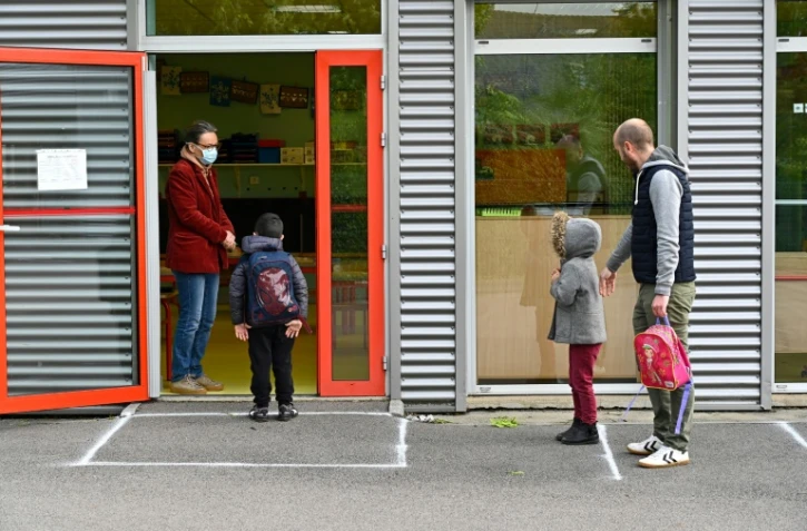 Un enseignant portant un masque de protection accueille un enfant dans sa classe tandis qu'un autre attend à distance, le 12 mai 2020 à l'école publique Champ l'Evêque de Bruz