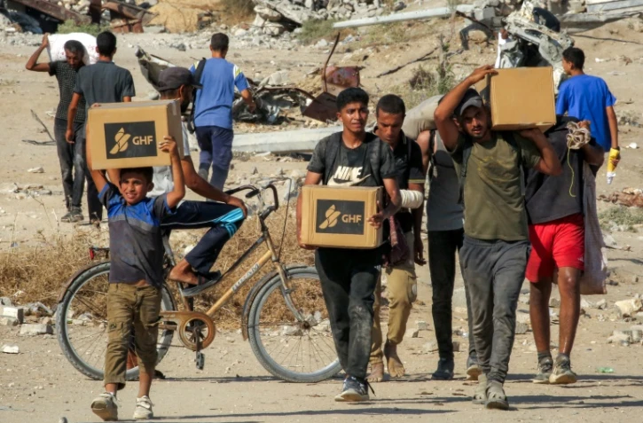 Des Palestiniens portent des cartons d'aide humanitaire reçus dans un centre de distribution géré par la Fondation humanitaire de Gaza (GHF), alors qu'ils traversent le "corridor de Netzarim", dans le centre de la bande de Gaza, le 22 août 2025
