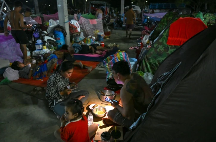 Une famille déplacée par les combats prend un repas en s'éclairant avec une lambe de poche dans un camp de la province de Banteay Meanchey, au Cambodge, le 12 décembre 2025