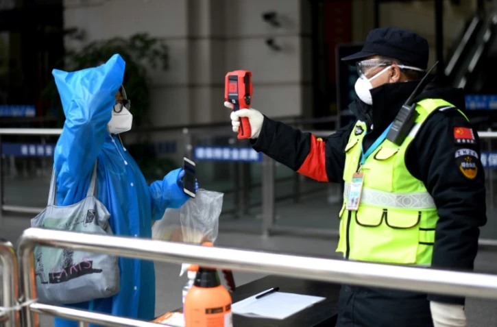 Une voyageuse portant un masque et une combinaison de protection contre le coronavirus passe au contrôle de la température à son arrivée à la gare Hankou, le 11 avril 2020 à Wuhan, dans la province chinoise du Hubei