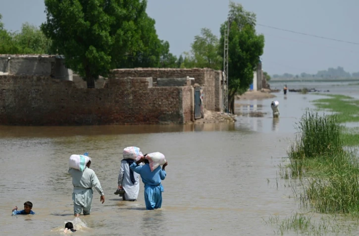 Des personnes touchées par les inondations traversent une zone submergée par les eaux de mousson, des sacs d'aide alimentaire sur le dos dans les faubourgs de Jacobabad, au Pakistan, le 6 septembre 2022