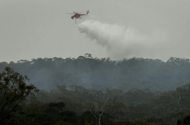 Un hélicoptère bombardier d'eau déverse son chargement sur un incendie, le 30 décembre 2019 dans une banlieue de Melbourne