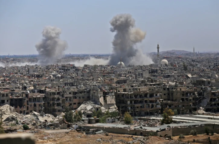 Photo prise le 24 avril 2018 lors d'un voyage de presse organisé par le gouvernement montrant de la fumée s'élevant de bâtiments dans le camp de réfugiés palestiniens de Yarmouk, près de Damas, lors de bombardements visant le groupe Etat islamique (EI)