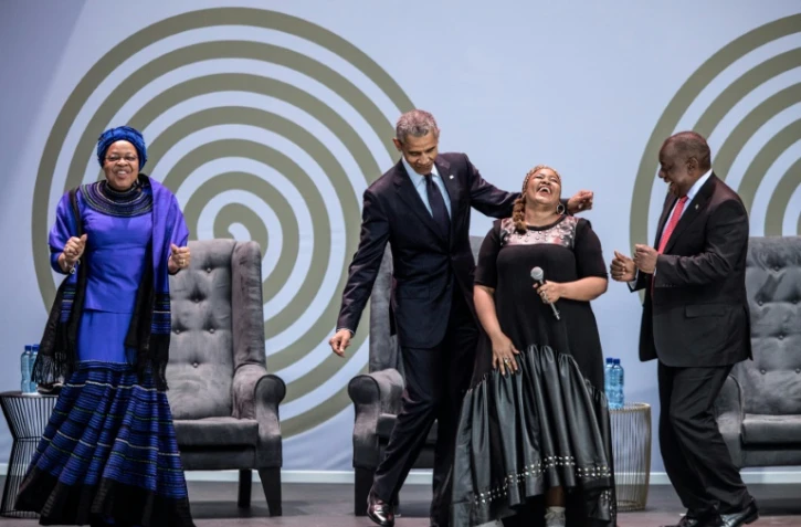 L'ex président américain Barack Obama, la veuve de Nelson Mandela, Graça Machel (à gauche) et le président sud-africain Cyril Ramaphosa (à droite) dansent en compagnie de la chanteuse Thandiswa Mazwai lors d'une cérémonie en l'honneur de Mandela, le 17 juillet 2018 à Johannesbourg