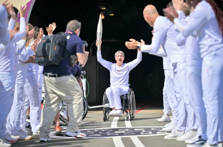 Emmanuelle Assmann, médaillée en escrime-fauteuil, brandit la flamme paralympique 
au terme d'une traversée inédite par le tunnel sous la Manche, le 25 août 2024 à Coquelles dans le Pas-de-Calais