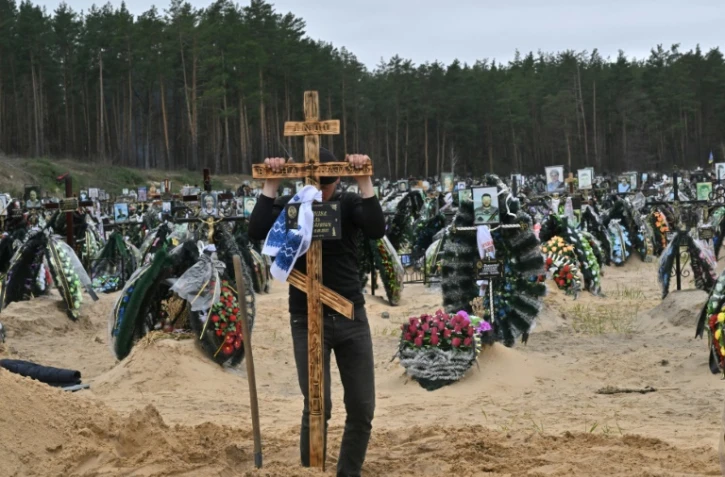 Un employé communal plante une croix sur une tombe pendant un enterrement à Irpin (Ukraine), dont le cimetière compte de nombreuses nouvelles sépultures, le 19 avril 2022