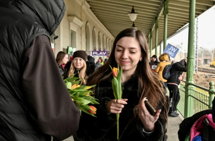 Une jeune femme sourit en recevant une tulipe offerte par un prêtre à l'occasion de la journée des droits des femmes, dans la gare de Przemyl (Pologne), où des centaines de réfugiés ukrainiens attendent une solution de relogement, le 8 mars 2022