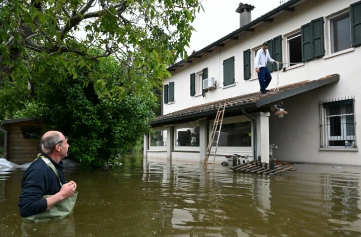 Un homme se sert d'une corde et d'une échelle pour sortir de sa maison inondée, le 20 mai 2023 à Ghibullo, près de Ravenne, en Italie