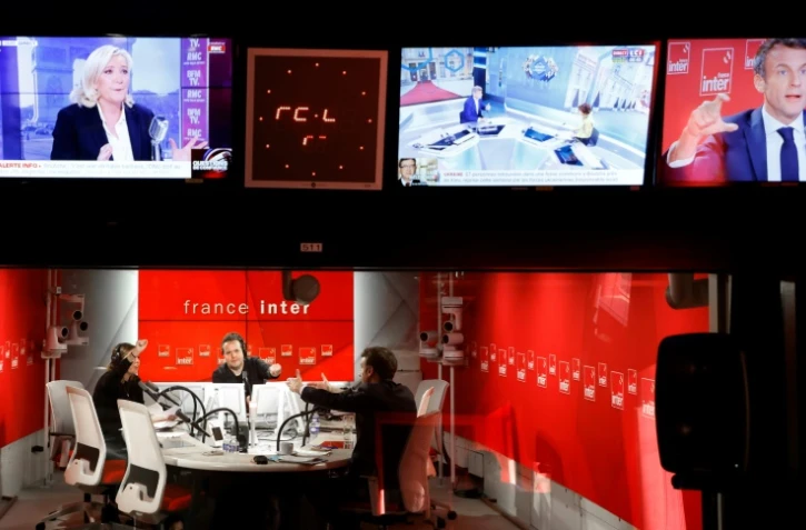 Le président français et candidat à sa réélection Emmanuel Macron répond aux questions de la journaliste Lea Salame (gauche) et du journaliste Nicolas Demorand (centre), sous un écran de télévision montrant la candidate du Rassemblement national à la présidentielle Marine Le Pen (en haut), lors d'une interview sur le 7/9, émission matinale de France Inter le 4 avril 2022 à Paris