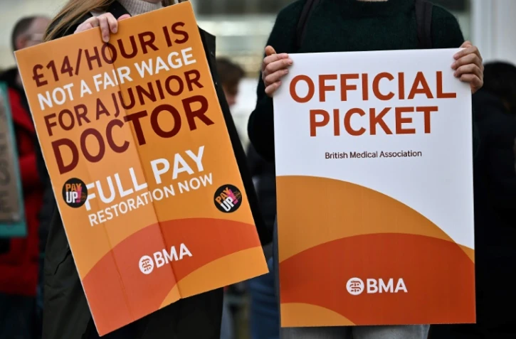 Des "juniors doctors" brandissent des pancartes réclamant de meilleurs salaraires du syndicat British Medical association lors d'un piquet de grève devant un hôpital de Londres le 20 décembre 2023